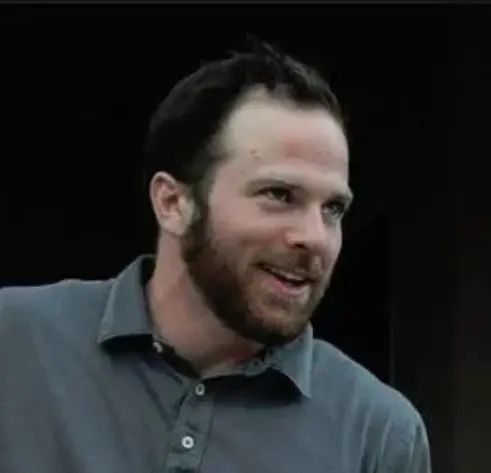 A man with a beard and mustache wearing a gray shirt.