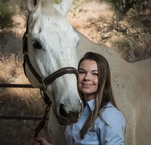 A woman standing next to a white horse.