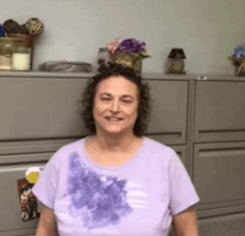 A woman in purple shirt standing next to cabinets.